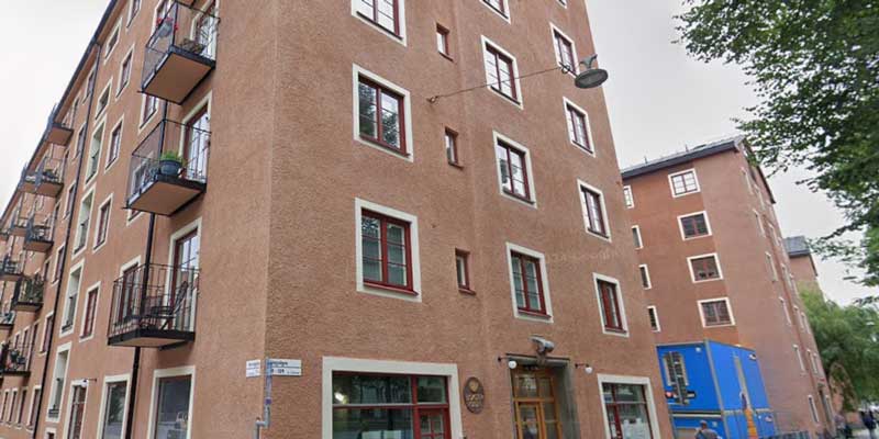 Fasad på ett rött putsat hyreshus i flera våningar med smårutiga fönster och franska balkonger