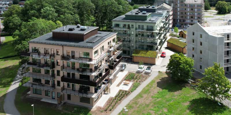 Flygfoto över nybyggda flerbostadshus med balkonger och planteringar, omgivna av grönska