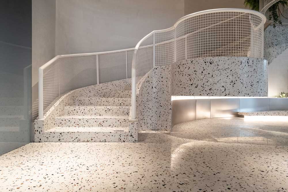 En elegant kurvad trappa i terrazzo med spräckligt mönster i beige och svarta prickar leder uppåt i ett modernt inomhusutrymme